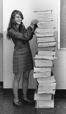 Margaret Hamilton se tenant auprès du code du logiciel de navigation qu'elle et son équipe ont produit pour le programme Apollo, janvier 1969. Par Draper Laboratory [Domaine Public], via Wikimedia Commons